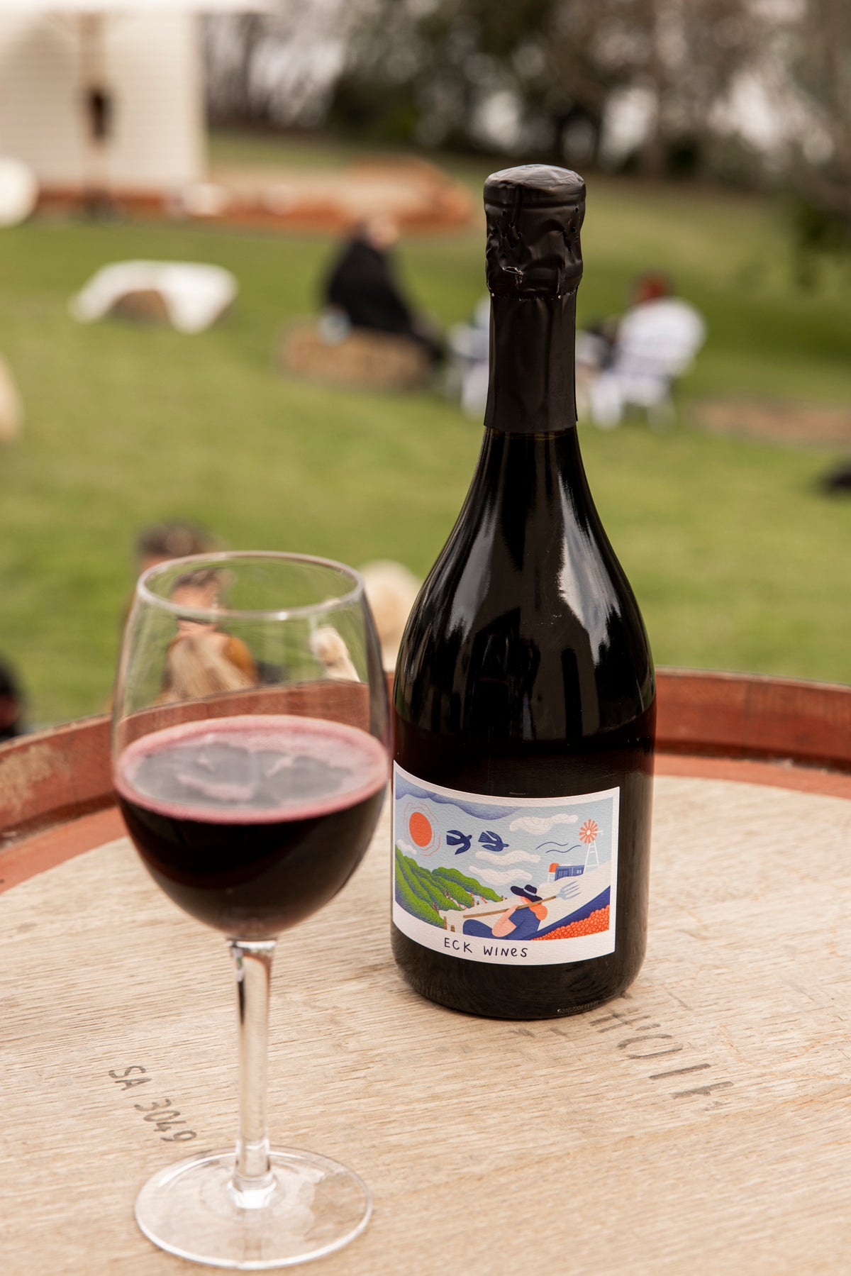 A bottle of ECK Wines and a glass of red on a wine barrel